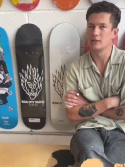Mikey sits on a bench with various new boards behind him.